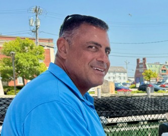 Captain David Grunes in a blue polo, smiling over his shoulder on a waterfront