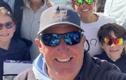 Captain Kerrick in a Sand Dollar cap and sunglasses, grinning with a boatload of guests behind him
