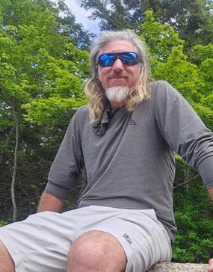 Captain Shawn Palmer seated outdoors in sunglasses against green trees