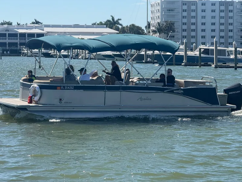 The Avalon pontoon cruising past a marina and waterfront condos on a sunny day