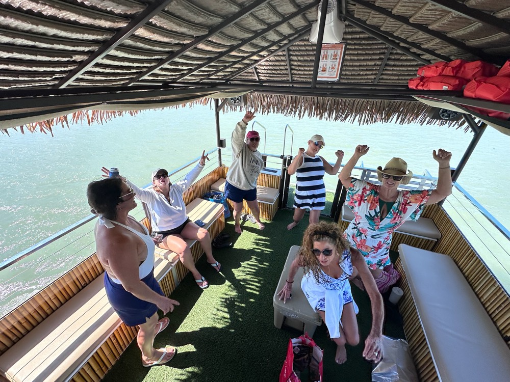 Group celebrating with raised hands and dancing aboard the Sand Dollar tiki boat for a birthday charter near Marco Island