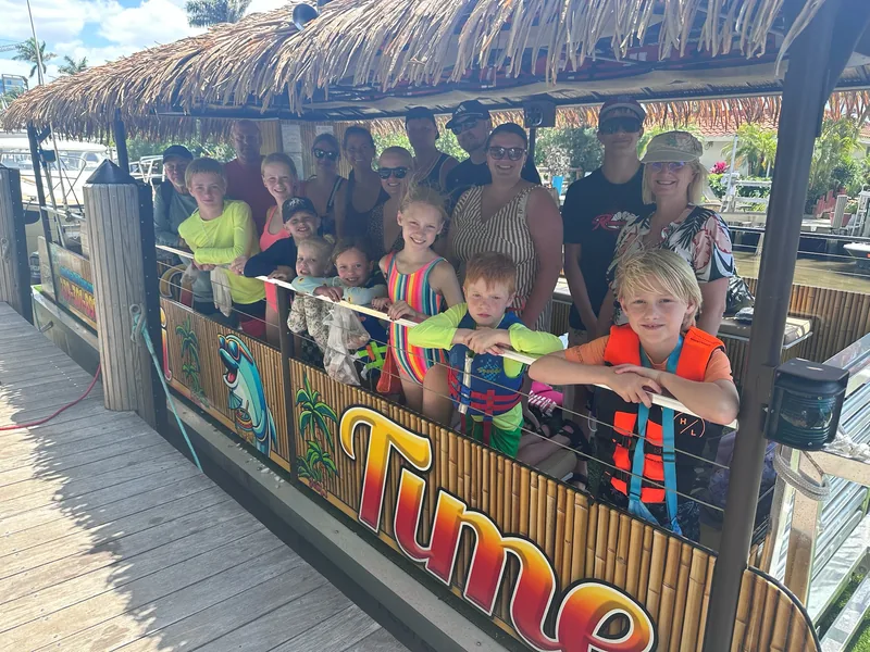 A big family group at the Tiki Time boat's rail at the dock, the youngest kids wearing bright life jackets