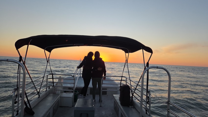 Couple silhouetted on the bow of a pontoon boat against a golden Gulf sunset on a Sand Dollar cruise, Marco Island