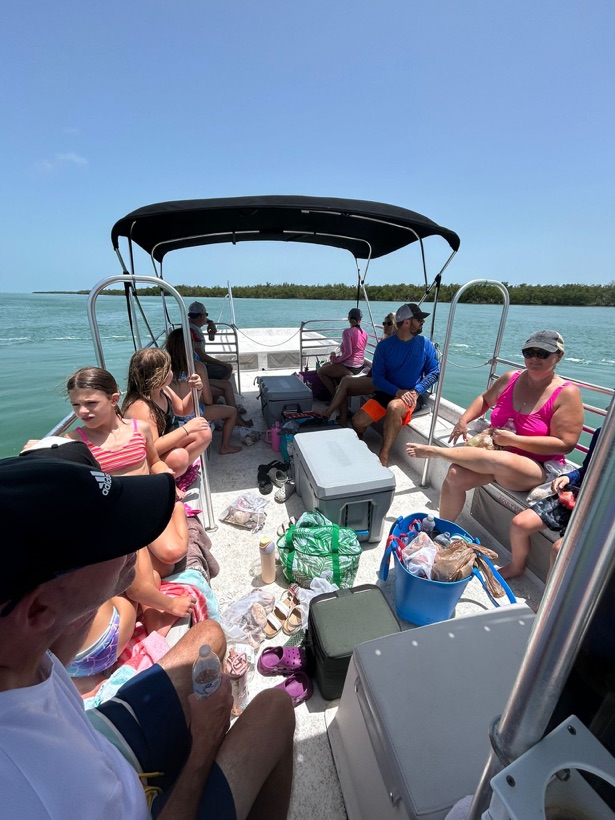 A family relaxing on their private Sand Dollar pontoon charter on bright blue water near Marco Island, Florida