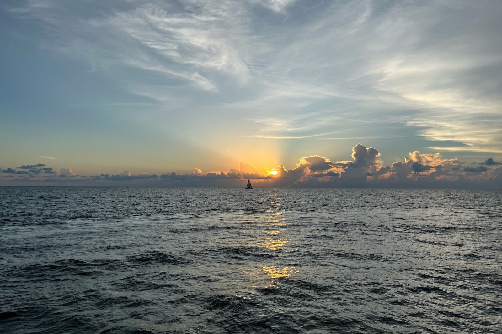 A fiery Gulf of Mexico sunset with a sailboat on the horizon, seen from a Sand Dollar sunset cruise