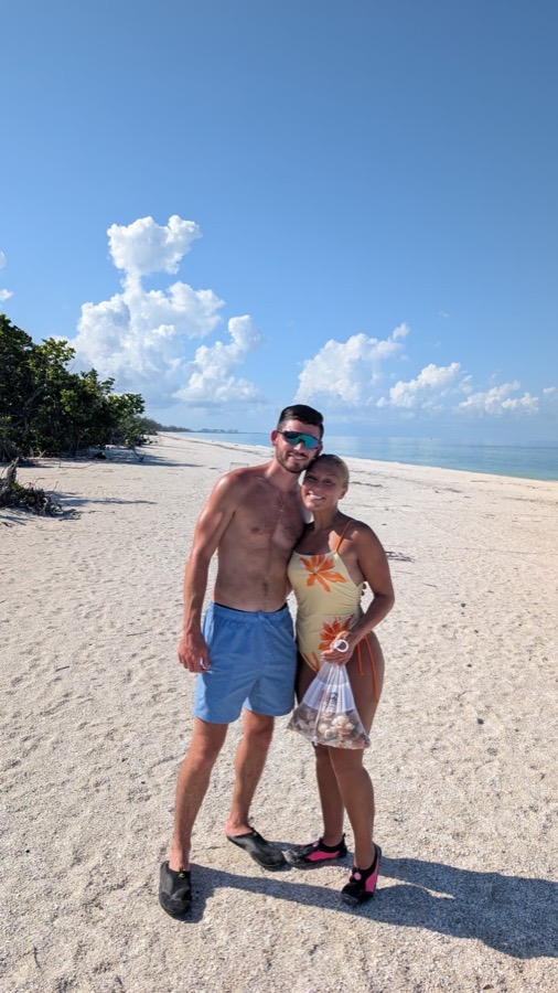 A couple on a white-sand beach holding a bag of shells from their Sand Dollar shelling tour