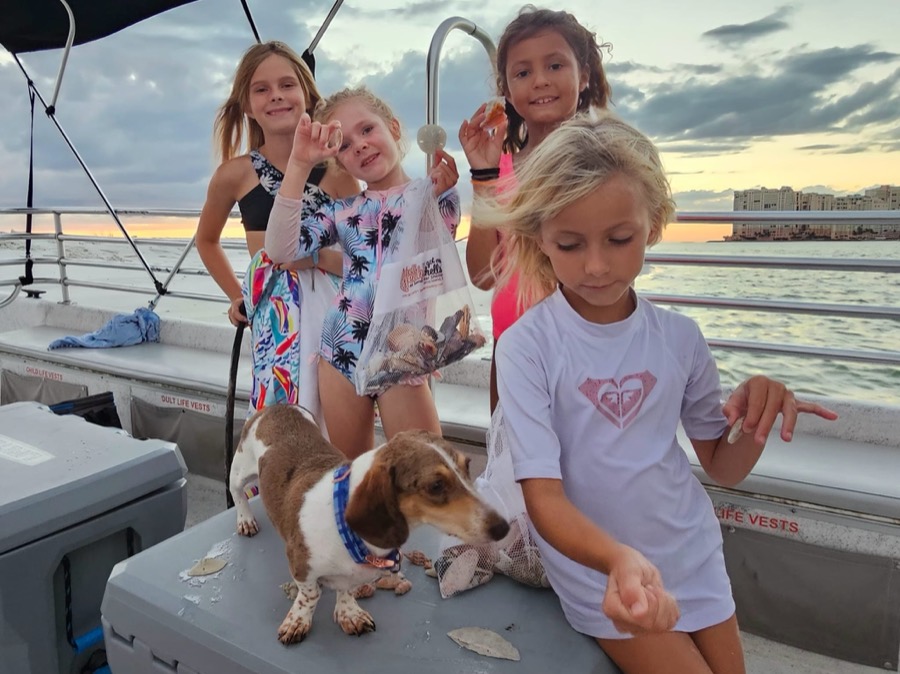 Guests and a dog displaying their shells aboard a Sand Dollar pontoon boat at sunset