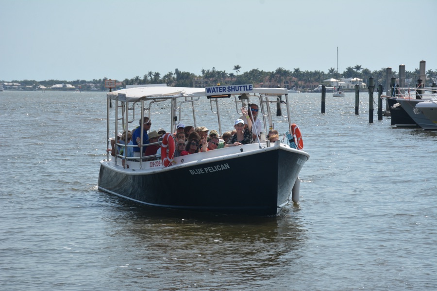 The Blue Pelican water shuttle head-on with its WATER SHUTTLE sign and a full deck of guests, Naples Bay