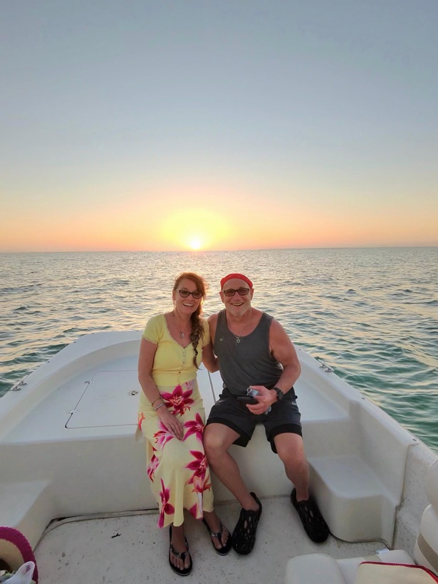 A couple smiling on the stern of a Sand Dollar boat in golden sunset light near Marco Island, Florida