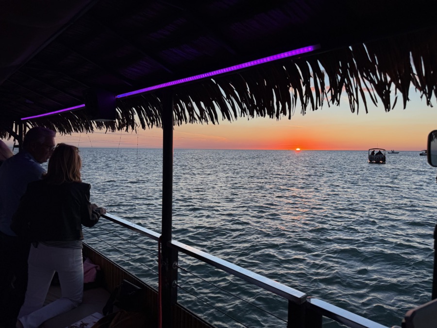 Guests watching a fiery red sunset from a Sand Dollar tiki boat with purple LED lights, Marco Island