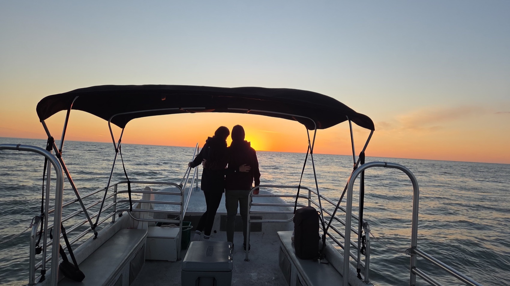 A couple silhouetted on the bow of a Sand Dollar boat against a golden Gulf sunset near Marco Island, Florida
