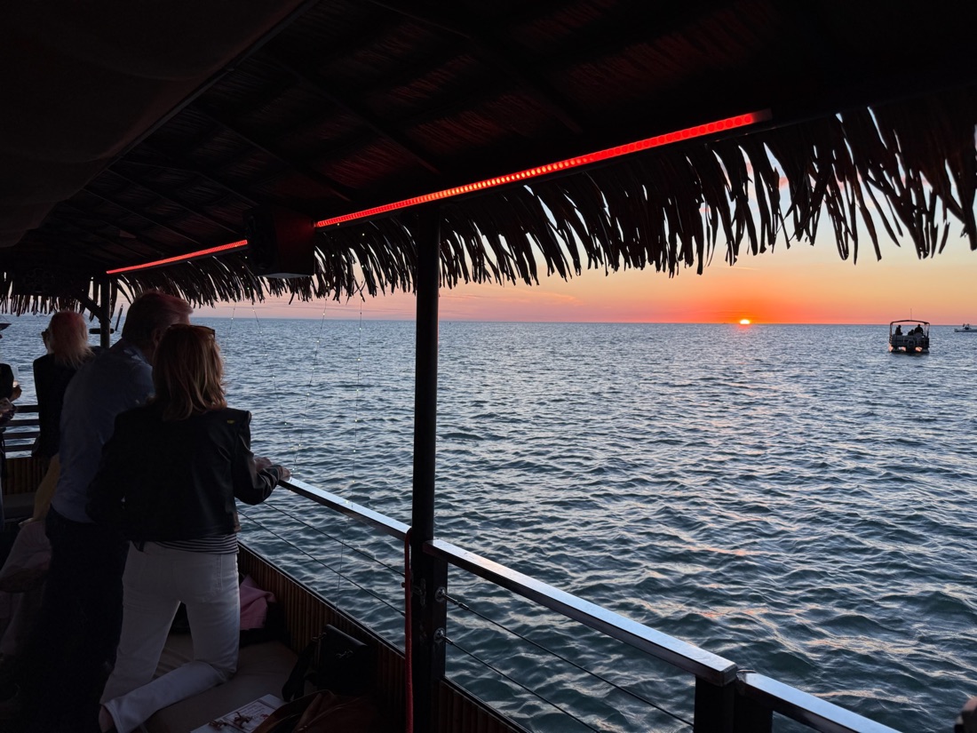 Guests at the rail of a Sand Dollar tiki boat watching a brilliant red-orange Gulf sunset near Marco Island, Florida