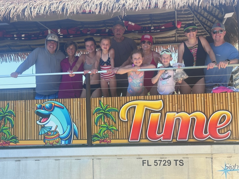 Kids and families lined up along the Tiki Time rail above the boat's cartoon dolphin artwork